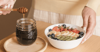 honey being drizzled on a fruit bowl for a breastfeeding mother